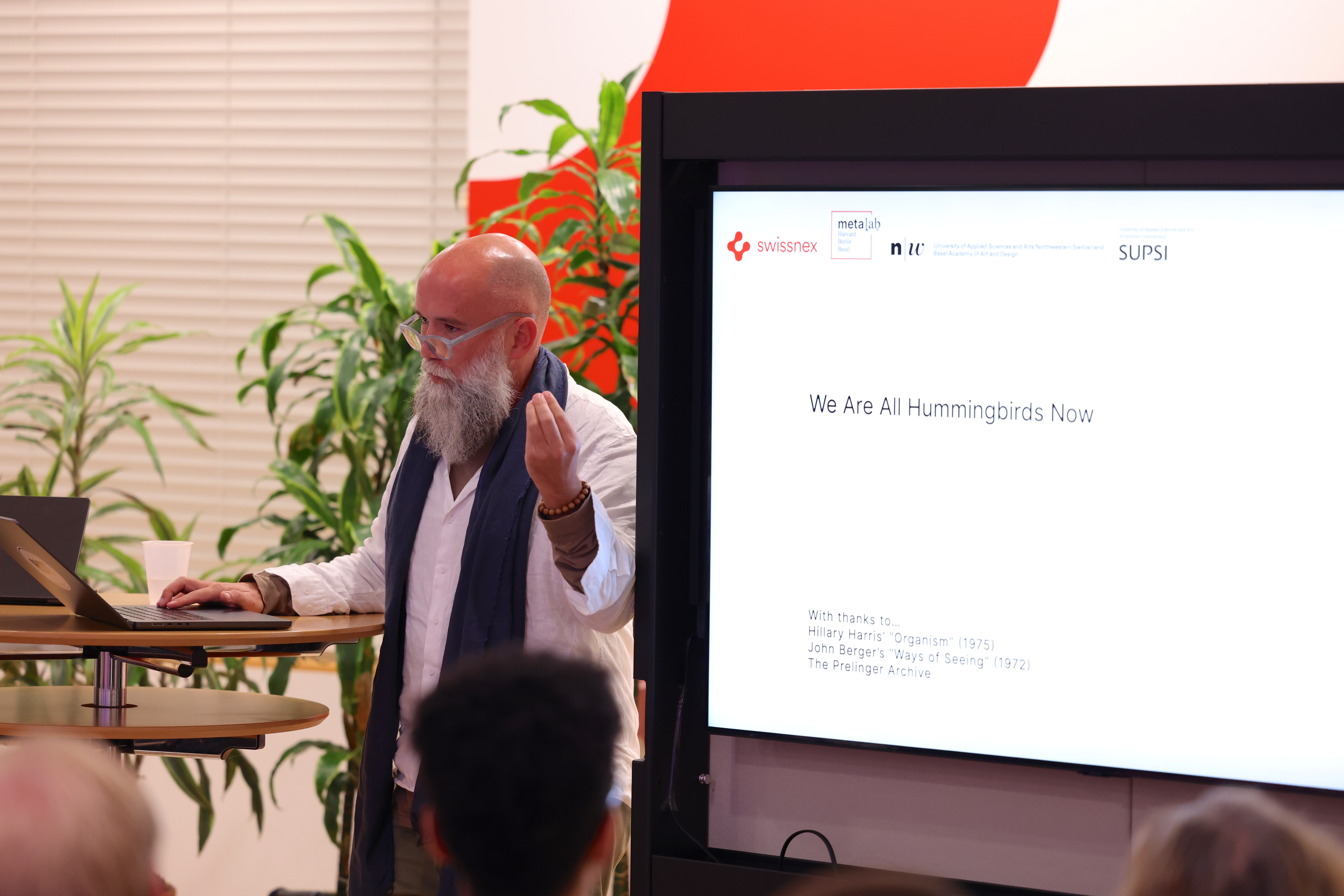 Speaker presenting with 'We Are All Hummingbirds Now' slide